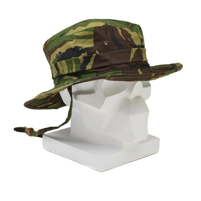Auténtico sombrero boonie militar holandés con camuflaje DPM, ala ancha, solapa para el cuello y correa ajustable para la barbilla en cabeza de maniquí blanca.