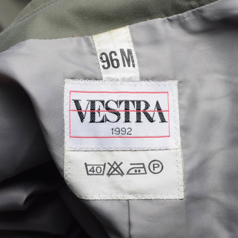 Close-up of Vestra 1982 clothing label with size 96M and care instruction symbols inside olive military raincoat