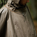 Close-up of a person wearing a vintage German army waterproof olive rain poncho with hood in a forest setting.