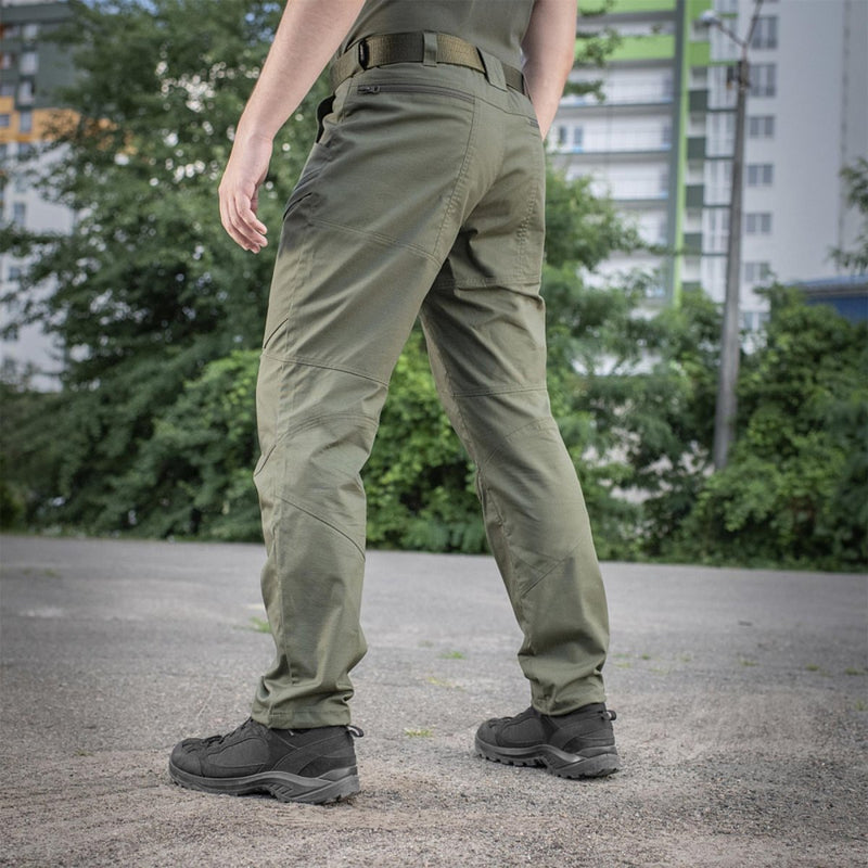 Back view of olive M-TAC military tactical pants with reinforced stitching worn outdoors on concrete ground.
