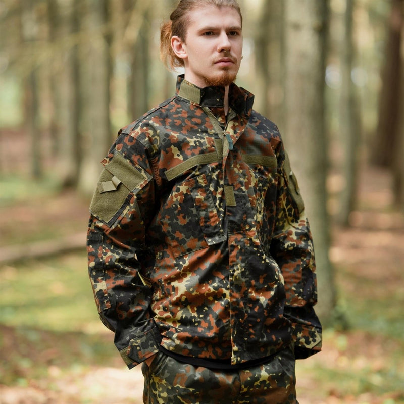 Man wearing MFH Brand U.S. Military style flecktarn camo ripstop jacket in forest setting with hands in pockets
