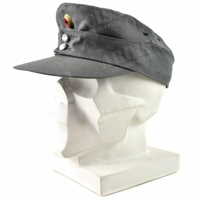 Gorra de montaña original del ejército alemán en gris con frente puntiagudo e insignia de metal en una cabeza de maniquí blanca.