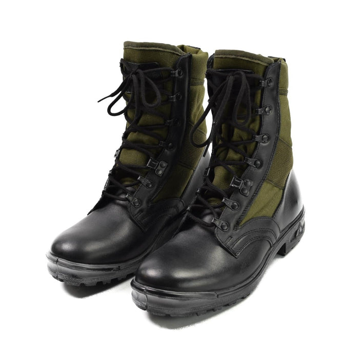 Par de botas tropicales del ejército alemán en negro y verde oliva con cordones y cremalleras laterales sobre fondo blanco.