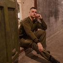 Man wearing olive green original Italian army Commando jumper sweater sitting indoors by rustic wall.