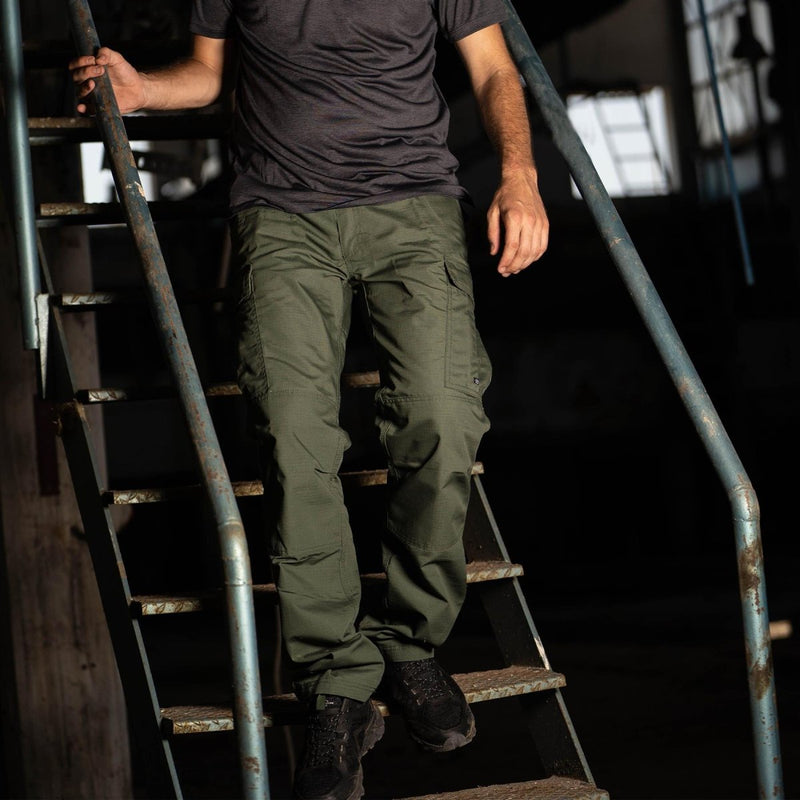 Man wearing olive green Pentagon BDU 2.0 combat cargo pants with reinforced knees and multiple pockets on metal stairs
