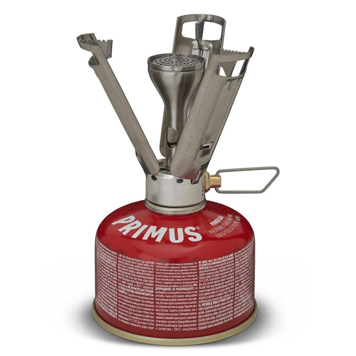 Estufa de camping ligera Primus Firestick Titanium montada sobre un recipiente de gas rojo con soportes para ollas desplegados.