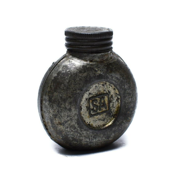 Botella de tinta de metal vintage con el logo 'SA' sobre un fondo blanco